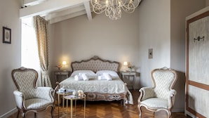 Een slaapkamer met een groot bed, twee nachtkastjes, een kroonluchter en twee fauteuils.
