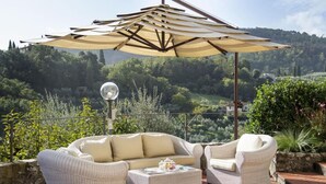 Een terras met rieten meubilair, een tafel en een grote parasol.