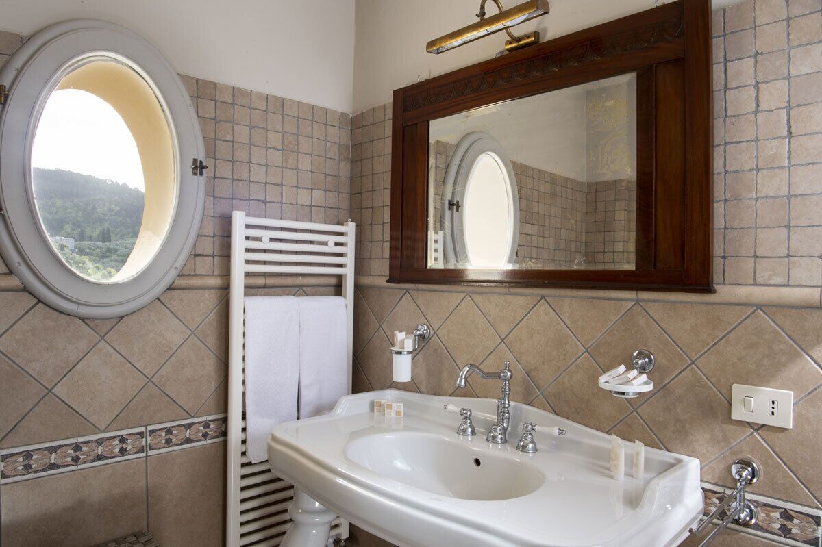 A bathroom with a large oval mirror, a white sink with two faucets, and a towel rack.