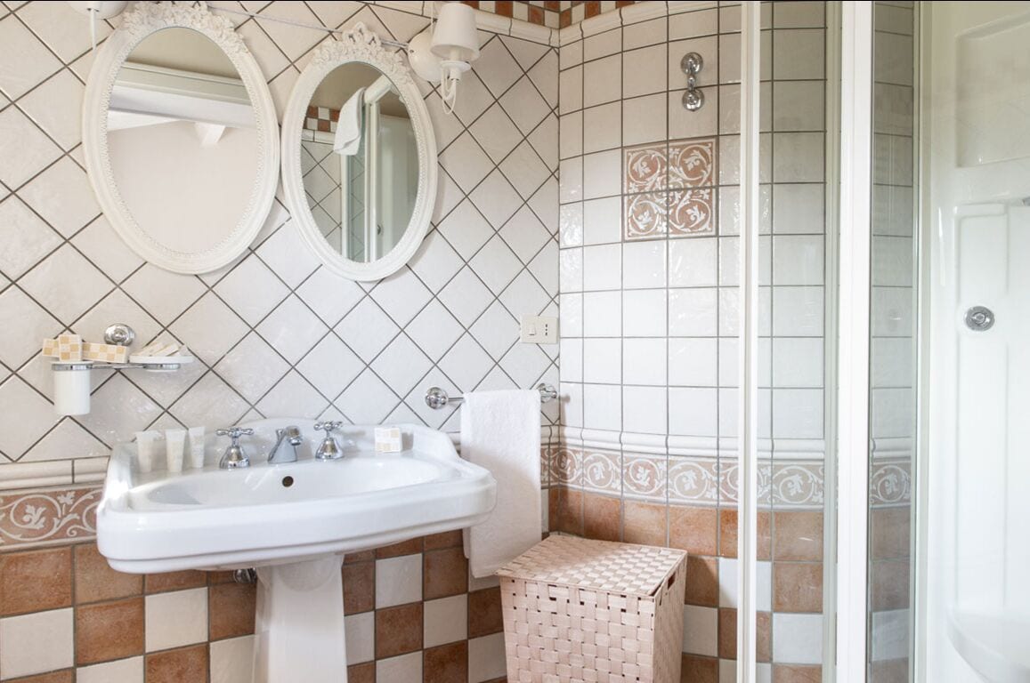 Un baño con un lavamanos blanco, dos espejos redondos y azulejos estampados.