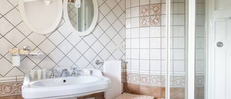 Un baño con un lavamanos blanco, dos espejos redondos y azulejos estampados.