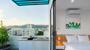 A balcony with a sink and a small kitchen area, a bed with white bedding, and a wall-mounted air conditioner. - Dandelion Apartment (Da Nang)