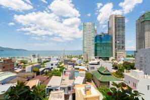 A coastal cityscape with various buildings, including a tall glass skyscraper under construction and several residential structures. - Dandelion Apartment (Da Nang)