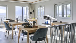 A modern dining area with wooden tables and grey chairs, large windows with curtains, and a view of the cityscape. - Kianga (Cape Town)