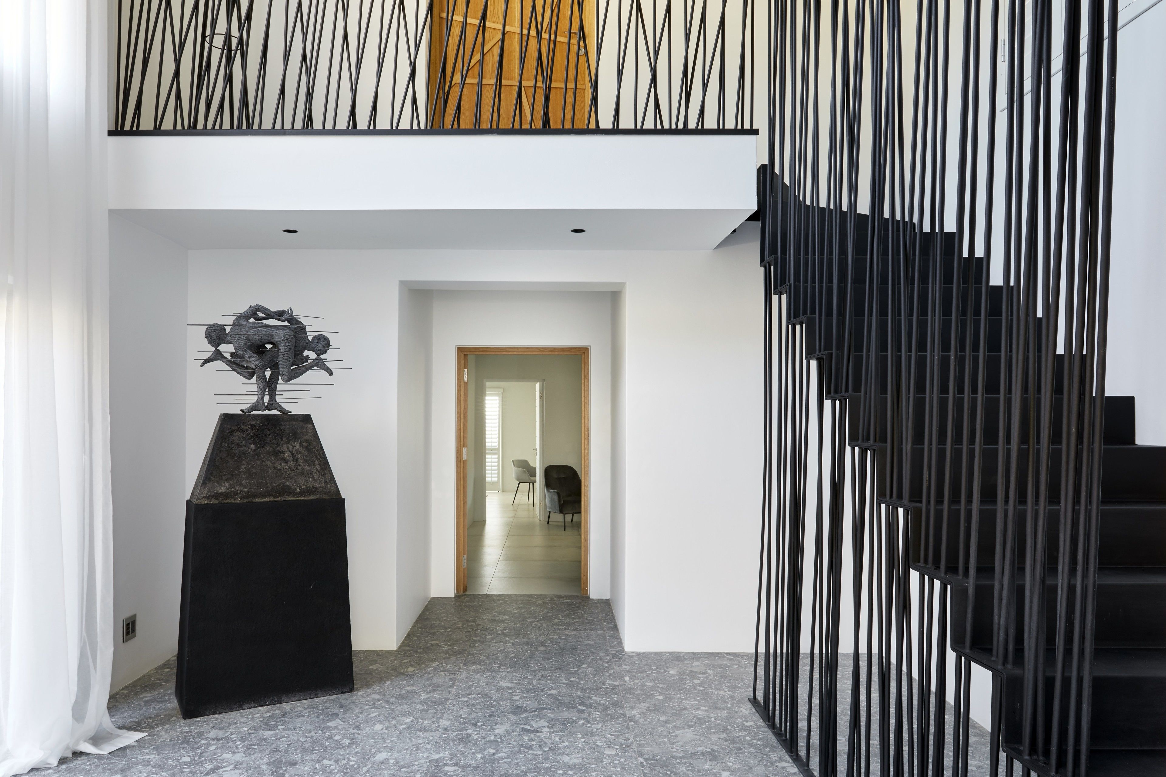 A modern interior with a black staircase, a geometric sculpture, and a view into a room with a wooden door.