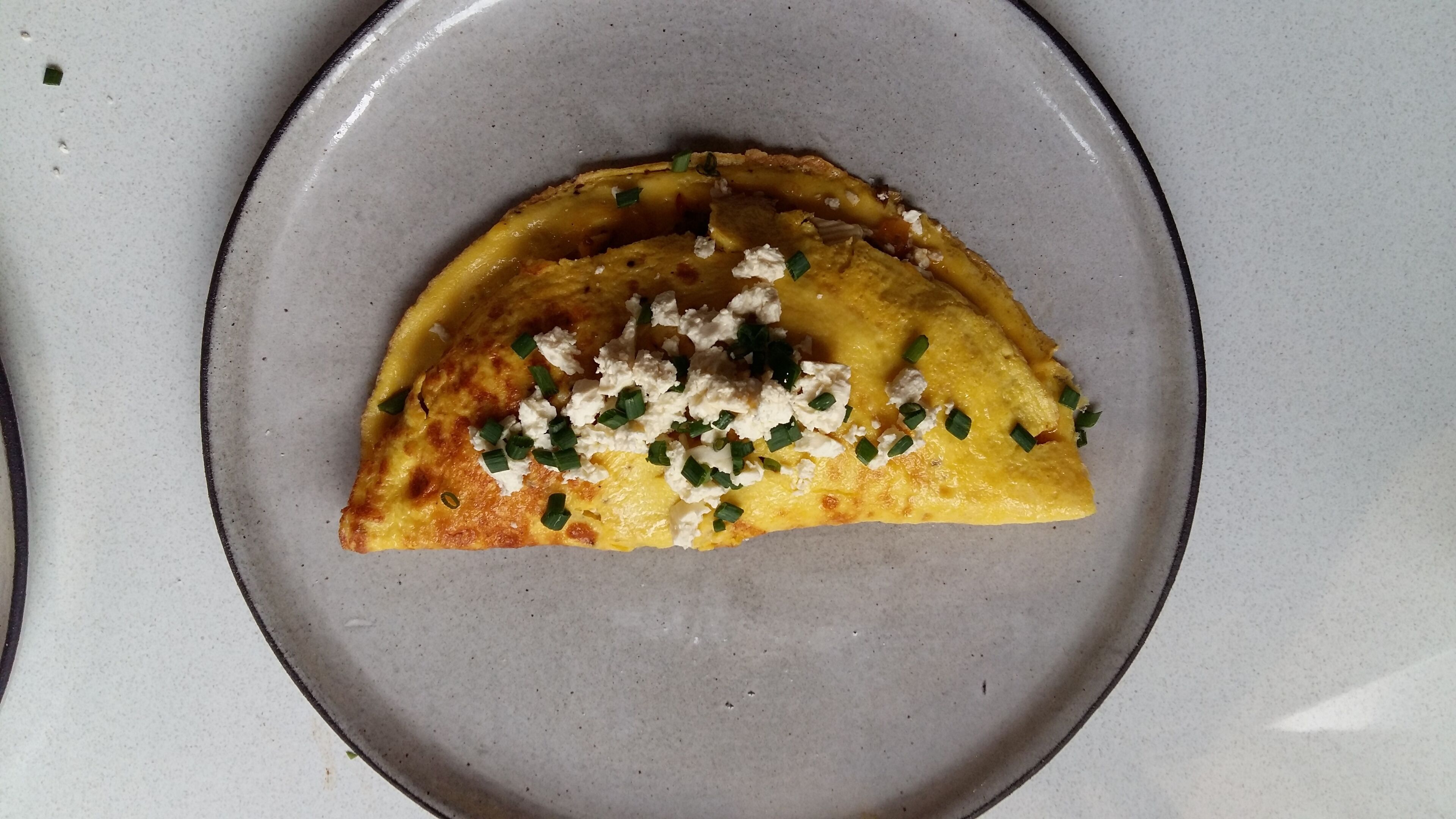 A plate with a half-moon shaped food item topped with crumbled cheese and green onions.