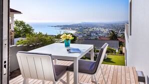 A balcony with a table and chairs, overlooking a coastal view with houses and the sea. - Kianga (Cape Town)