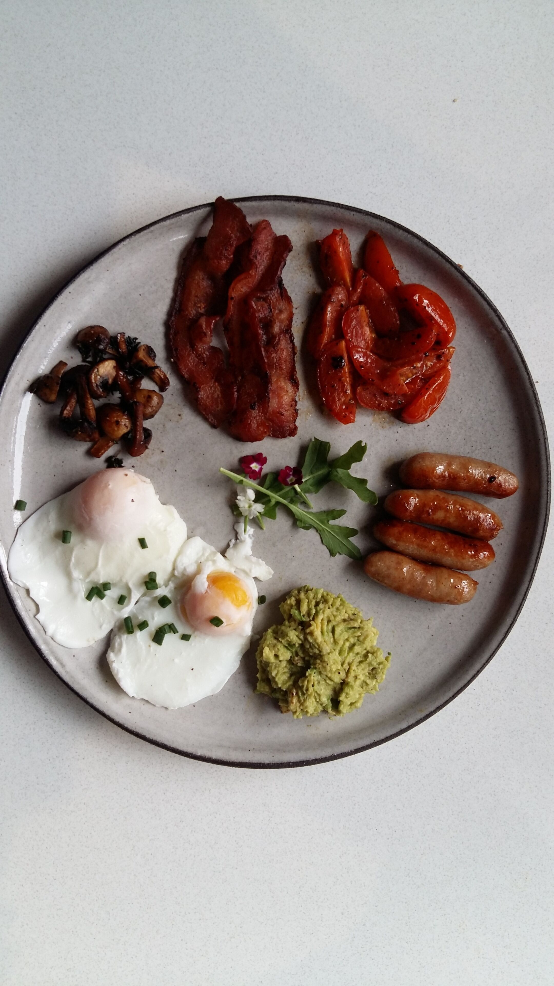 A plate with bacon, sausages, mushrooms, a poached egg, and avocado.