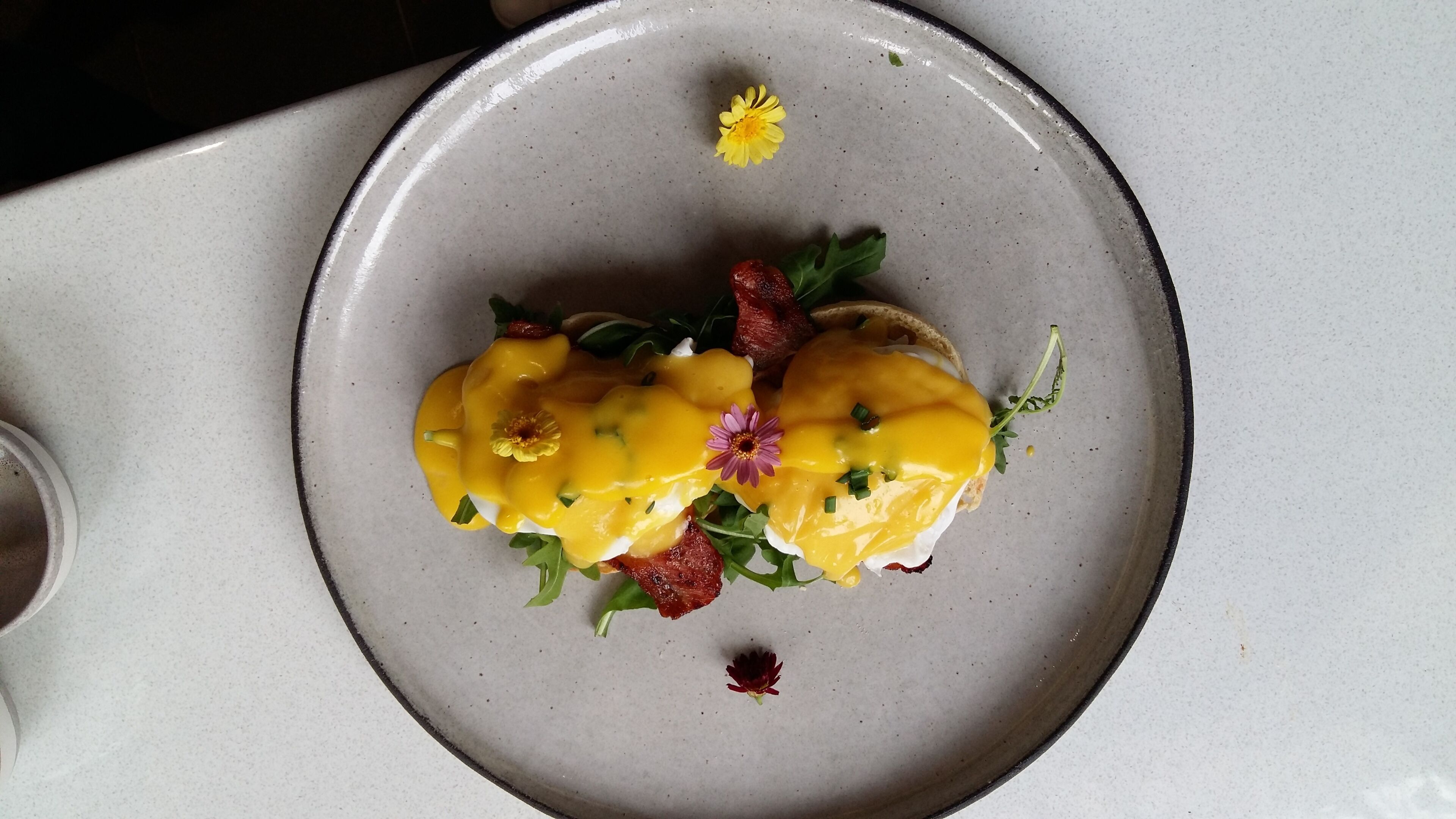 A plate with a dish of poached eggs, hollandaise sauce, and garnishes.