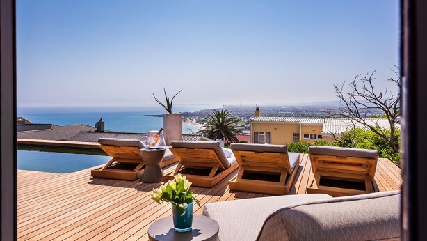 A wooden deck with lounge chairs and a small table, overlooking a coastal cityscape. - Kianga (Cape Town)