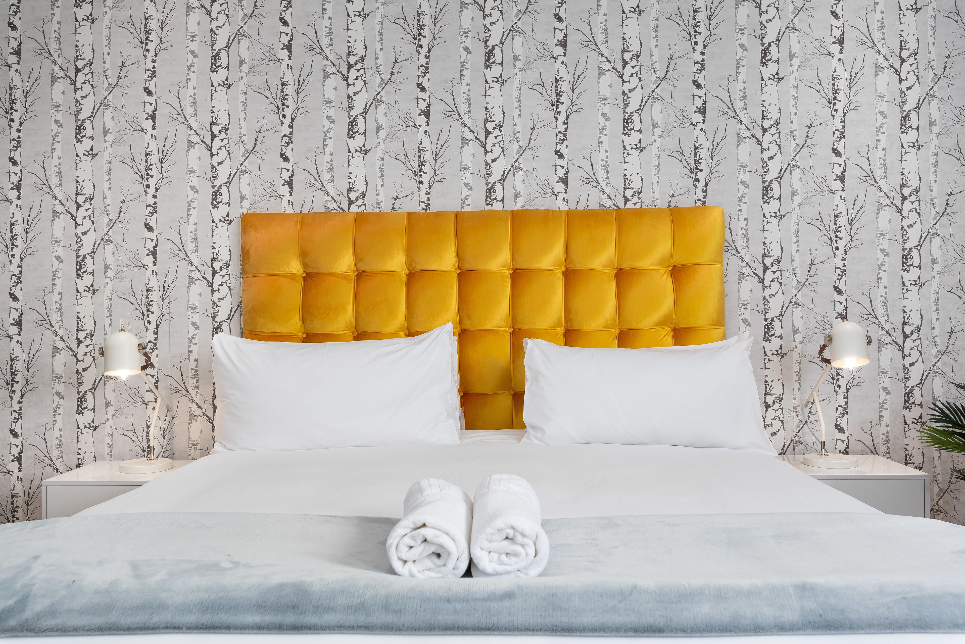 A neatly made bed with white linens, a yellow tufted headboard, and two bedside lamps.