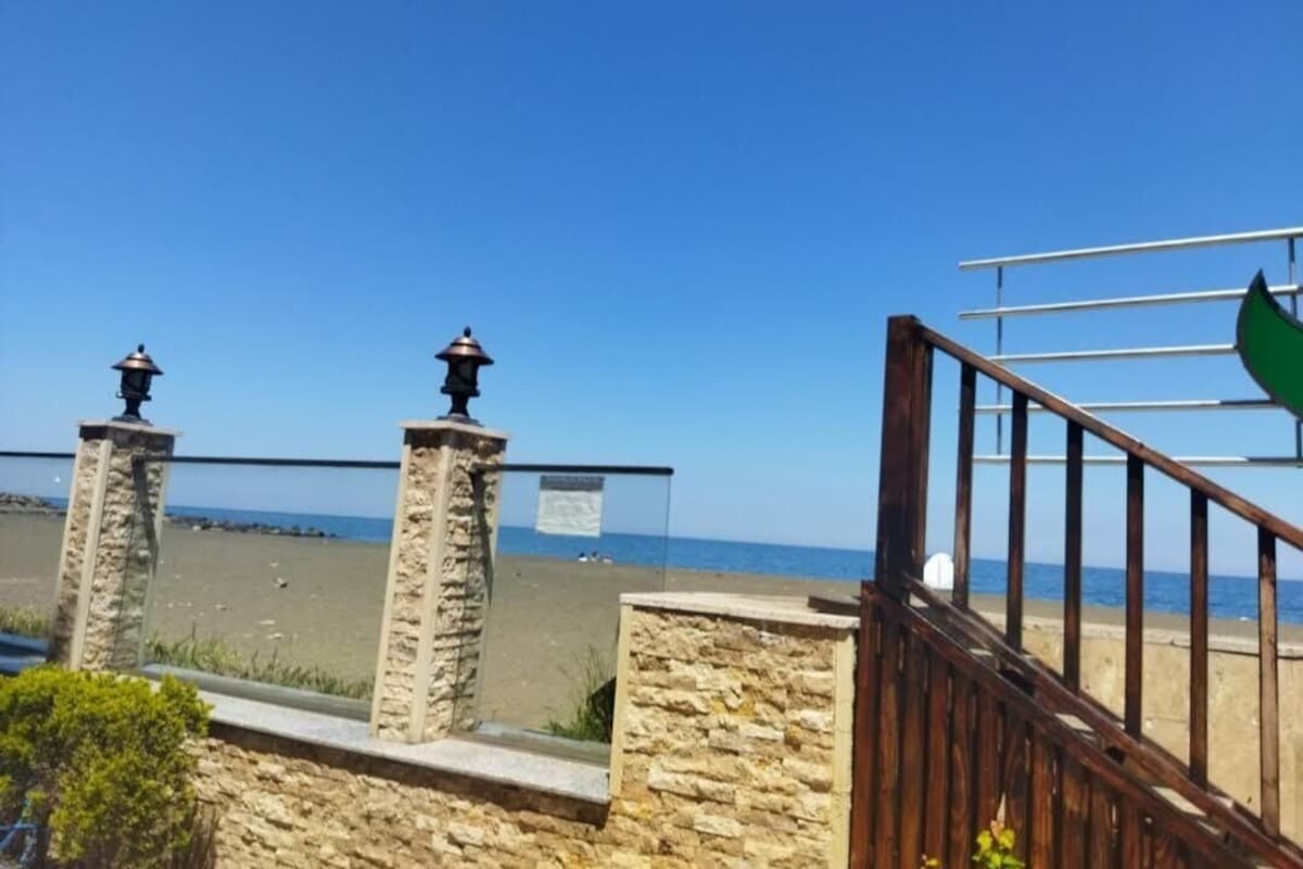 A stone wall with a metal gate and a beach in the background.