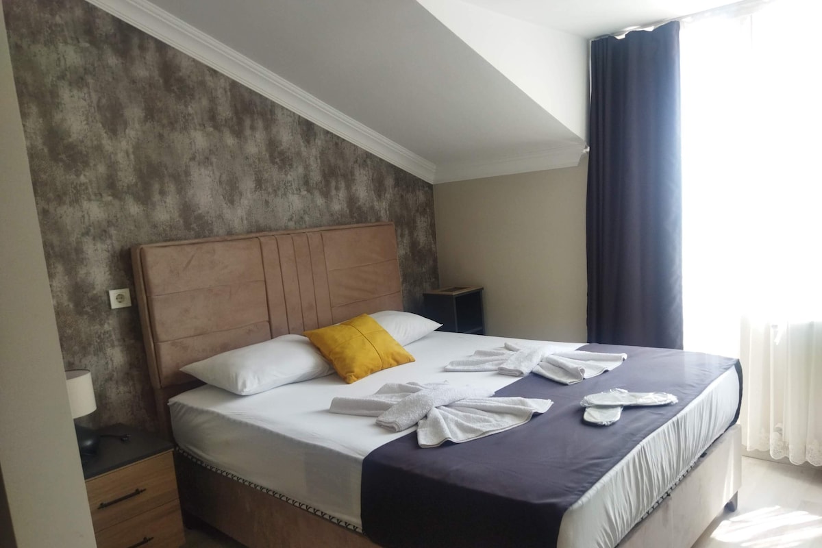 A neatly made bed with a wooden headboard, white and yellow pillows, and neatly folded towels.