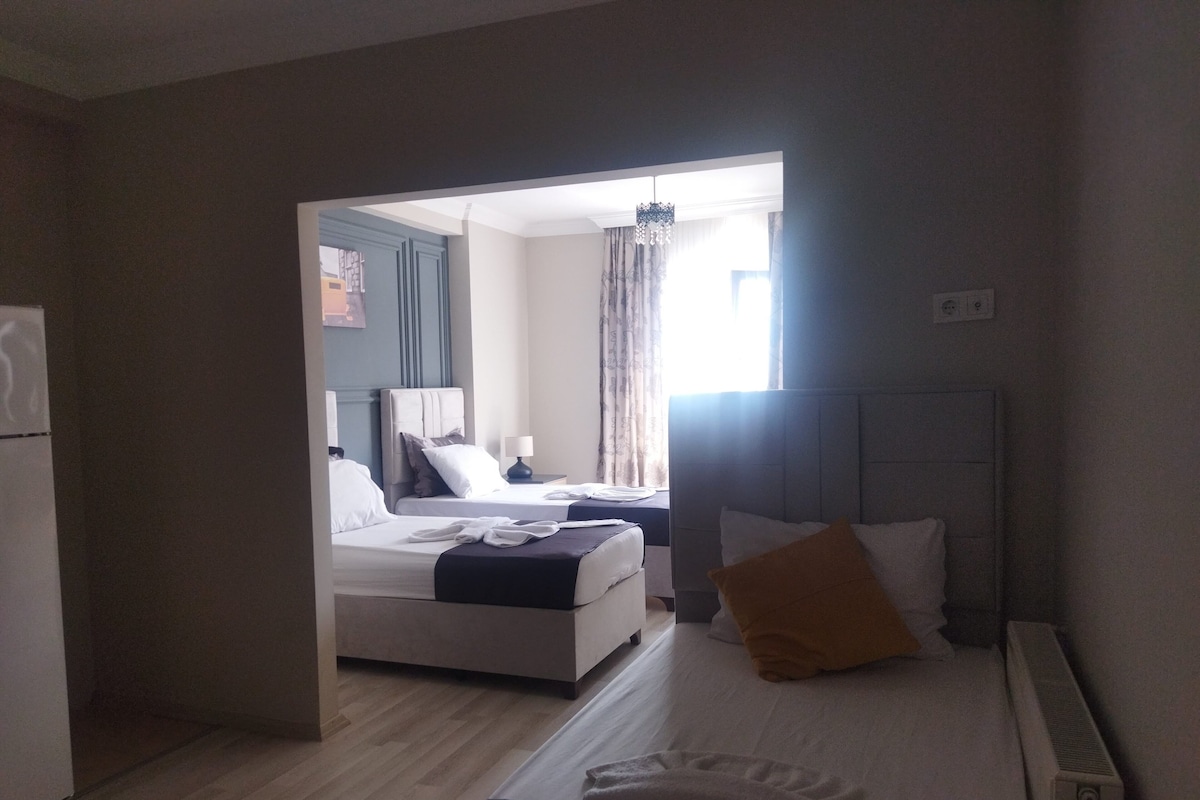 A hotel room with two beds, a window with curtains, a radiator, and a door leading to another room.