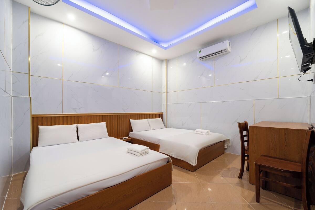 A hotel room with two beds, a wooden desk, a chair, and a TV.