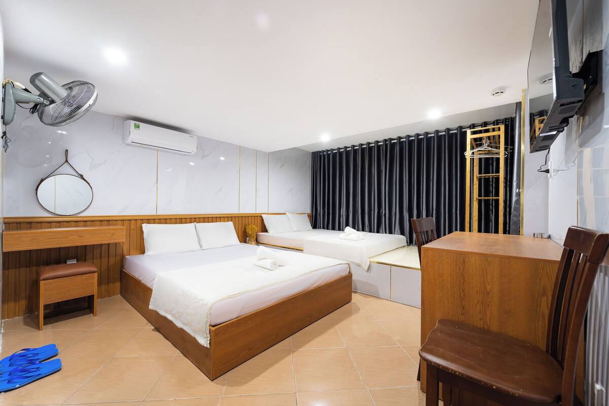 A hotel room with a wooden bed, a desk, a chair, a mirror, and an air conditioning unit.