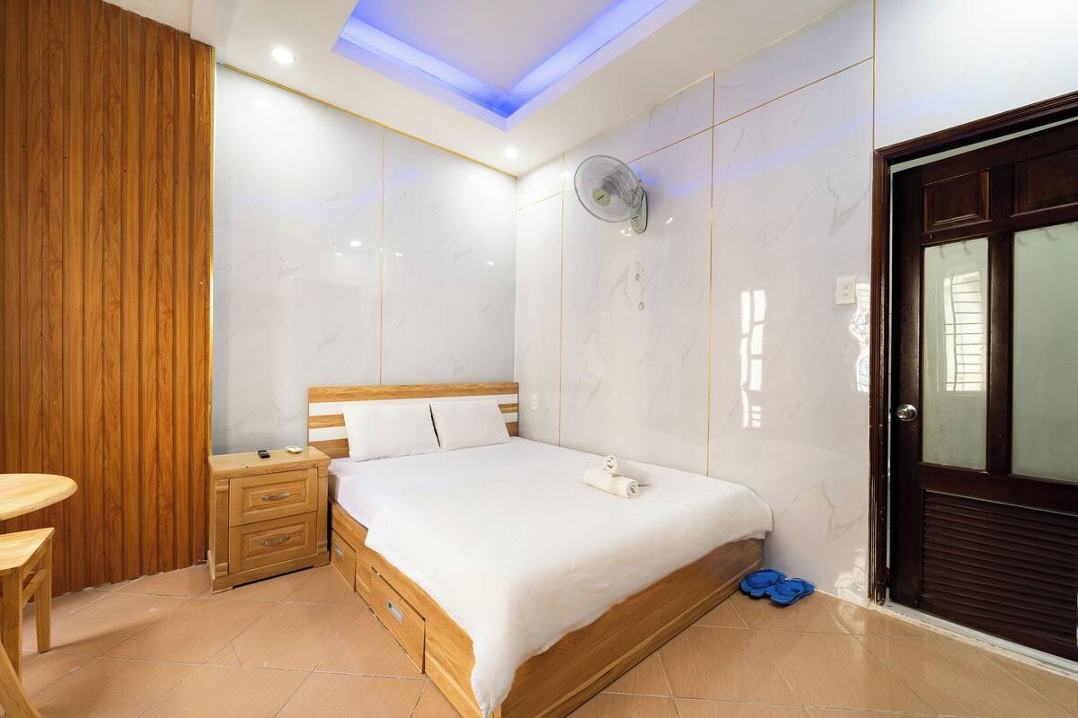 A bedroom with a wooden bed, a bedside table, a wooden wardrobe, and a ceiling fan.