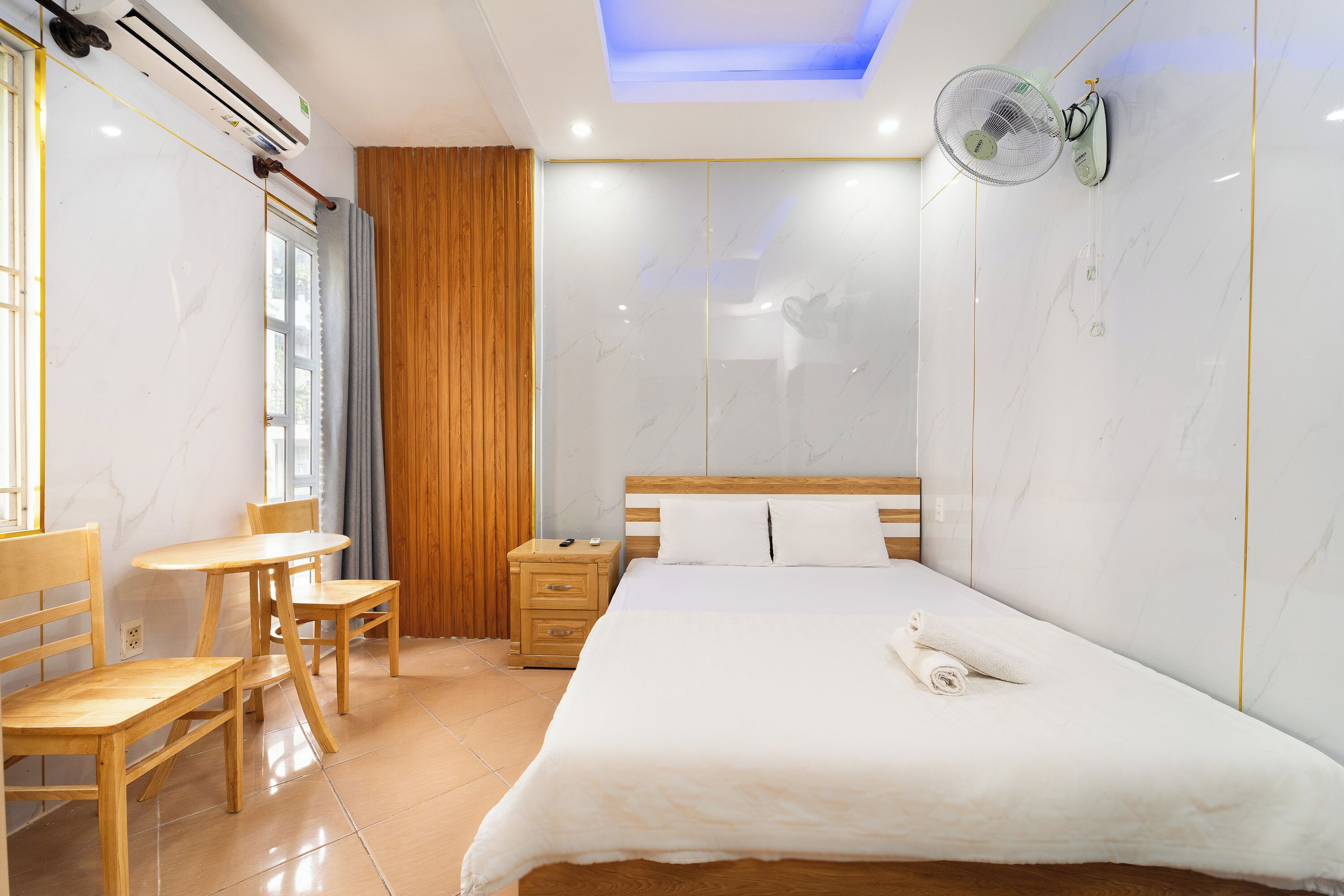 A hotel room with a bed, wooden furniture, a small table, and an air conditioning unit.