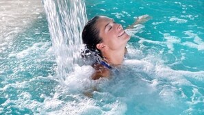 Una persona en una piscina con agua brotando de un caño metálico.
