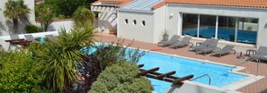 Una piscina con sillones de descanso, rodeada de palmeras y un edificio con tejado de tejas.