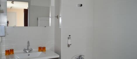 A bathroom with a white sink, two orange soap dispensers, a mirror, and a shower area.