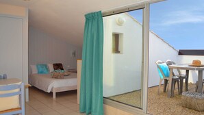 Un dormitorio con cama, una mesa y una silla, un balcón con mesa y sillas, y una ventana con cortina.