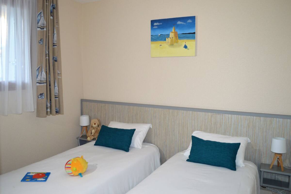 Quarto de hotel com duas camas, um quadro de uma praia, um urso de pelúcia e um brinquedo na mesa de cabeceira.