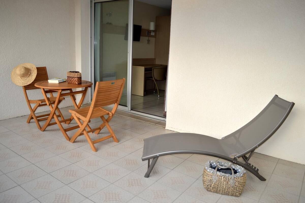 Uma varanda com mesa e cadeiras de madeira, uma poltrona e um cesto de fibra.