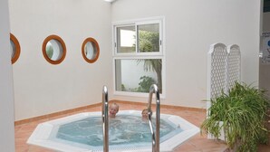 Un jacuzzi con barandillas de metal, una ventana con vistas a la vegetación y una división blanca con diseño de celosía.