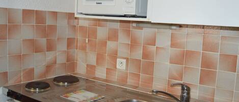 Una cocina equipada con microondas, dos hornillas, un lavamanos y salpicadero de azulejos.
