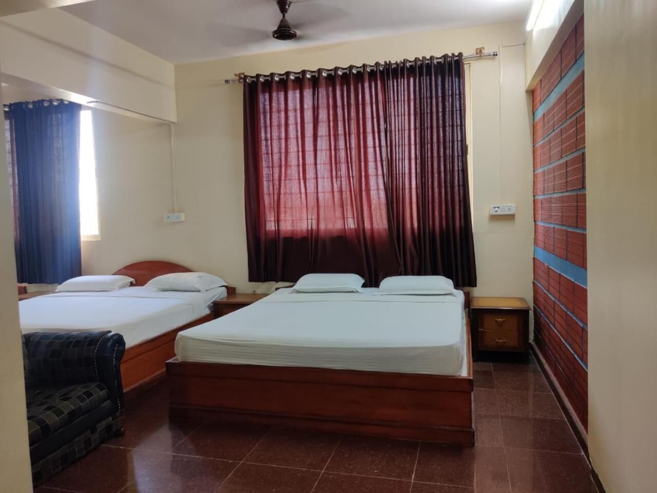 Habitación de hotel con dos camas individuales, un cabecero de madera, una mesita de noche pequeña, un armario y un ventilador de techo.