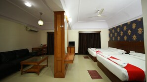 Quarto de hotel com sofá, mesa de centro de madeira, televisão, cama com manta vermelha e ventilador de teto.
