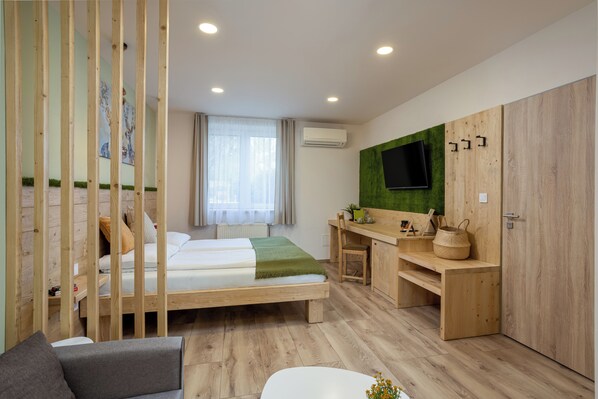 A room with a bed, a desk, a TV mounted on a green wall, and a wooden wardrobe.