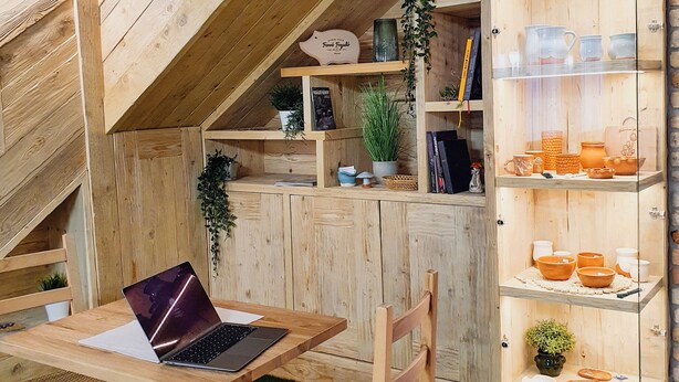 Interior de madera con una mesa, sillas y estantes mostrando cerámica.