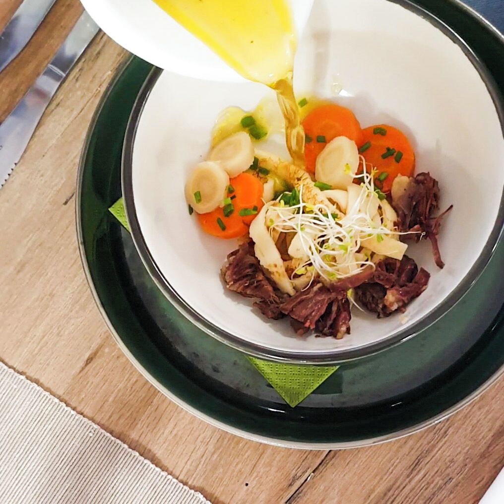 Un tazón de comida con varios ingredientes, incluyendo zanahorias, brotes y un líquido que se está sirviendo.