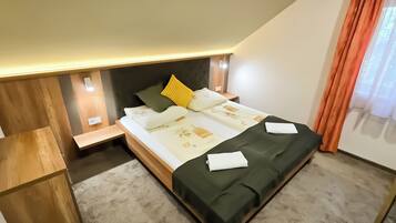 Un dormitorio con cama, mesitas de noche, una silla y una ventana con cortinas.