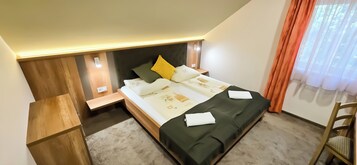 Un dormitorio con cama, mesitas de noche, una silla y una ventana con cortinas.