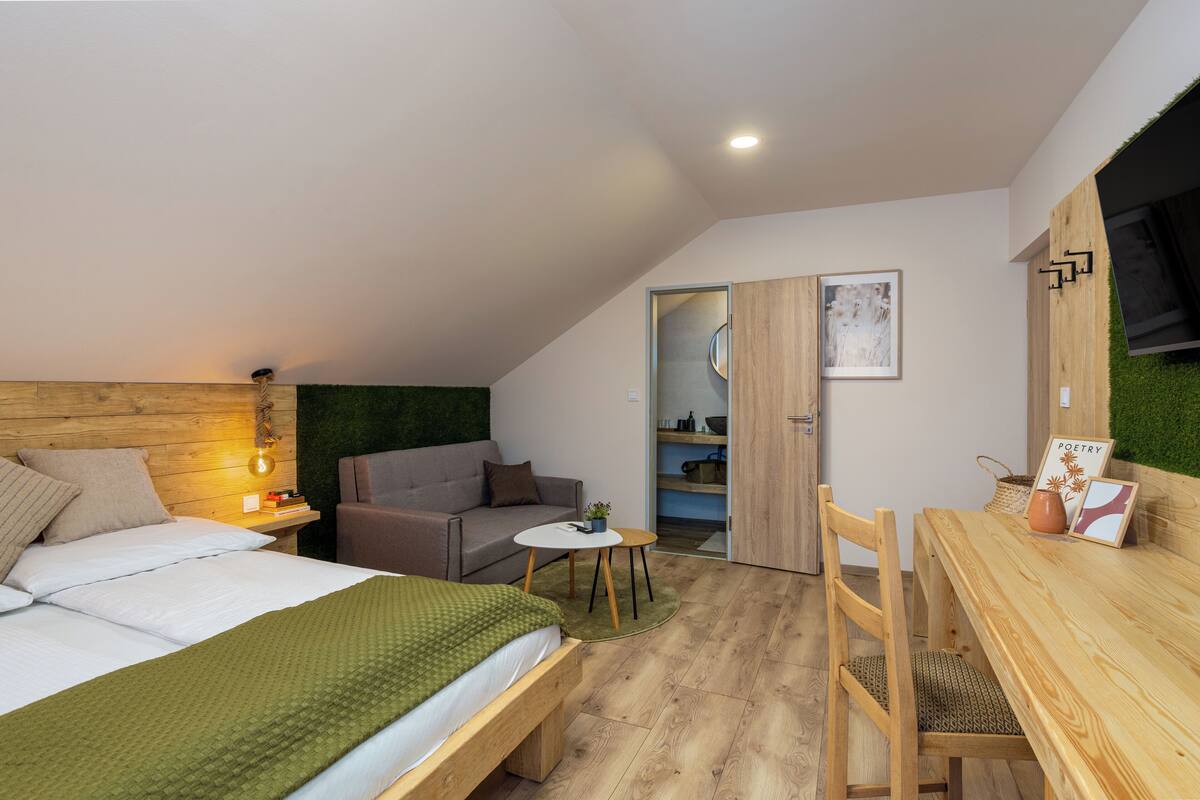 A modern bedroom with a bed, a small sofa, a wooden desk, and a green wall.