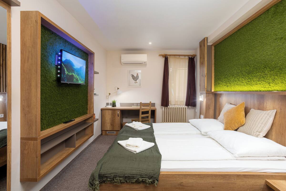 A hotel room with a bed, a desk, a television, and a green wall.