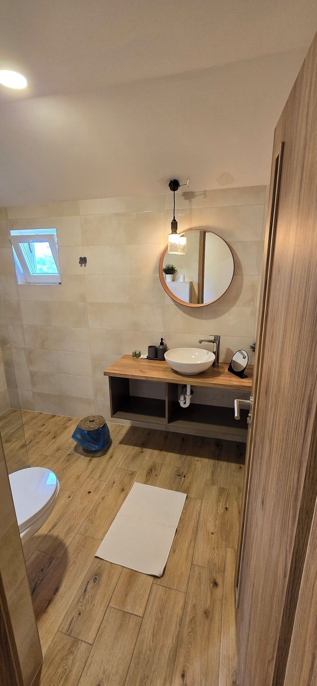A bathroom with a wooden floor, a round mirror, a sink, and a window.