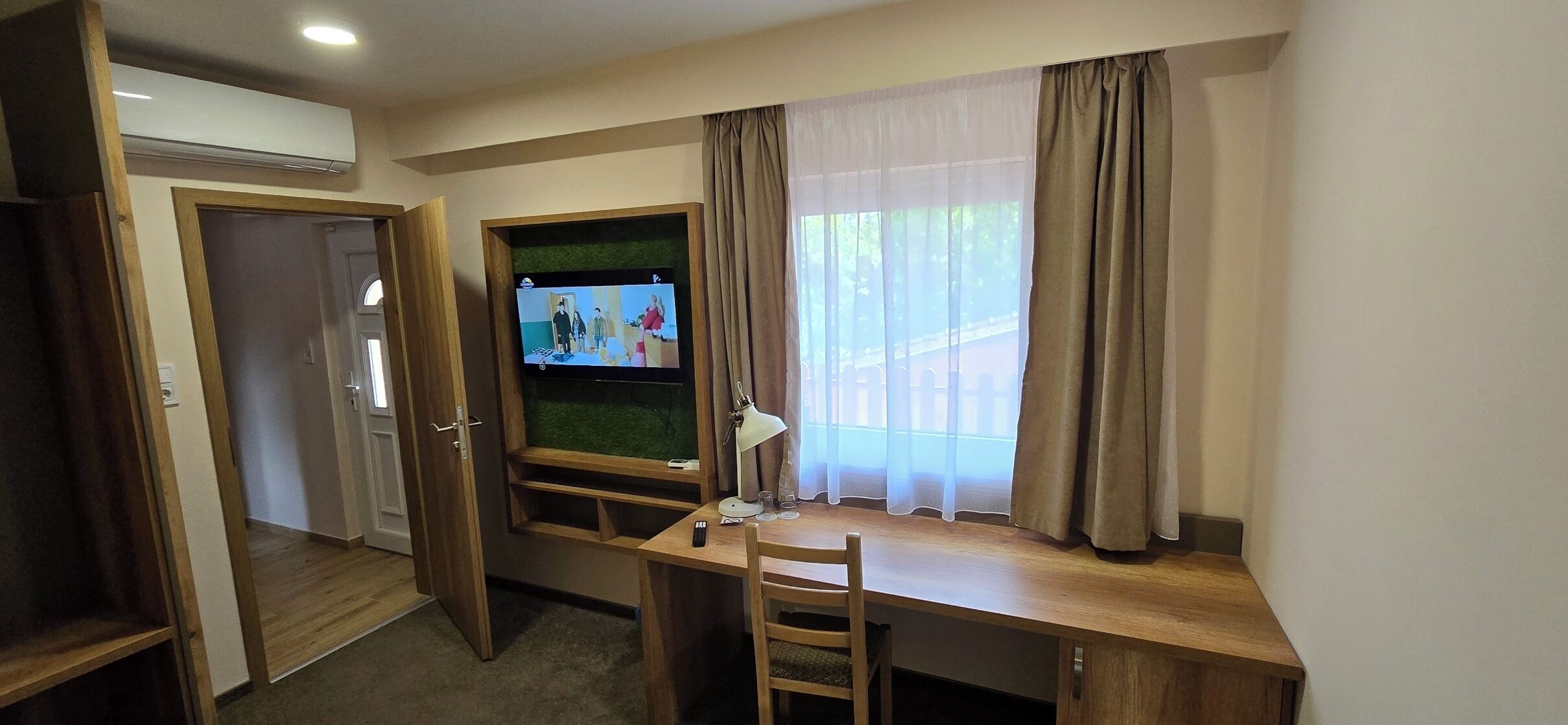Una habitación con escritorio, televisor, silla y ventana con cortinas.