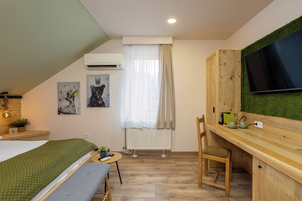 A bedroom with a bed, a desk, a chair, a radiator, a TV, and artwork on the wall.
