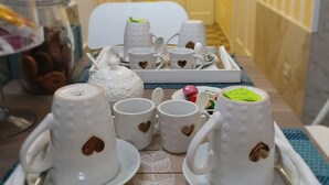 A tray with white ceramic cups and saucers, some with heart-shaped cutouts, on a wooden table with a blue placemat. - Lesuite Napoli (Naples)