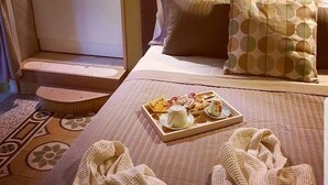 A hotel room with a bed, a tray of breakfast items, and a bathroom with a stone wall. - Lesuite Napoli (Naples)