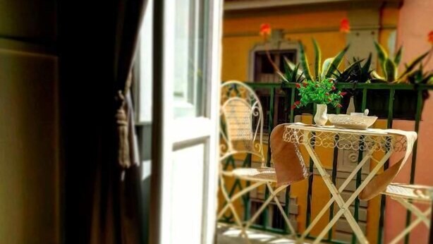 A balcony with a small table and chairs, a potted plant, and a view of a yellow building. - Lesuite Napoli (Naples)