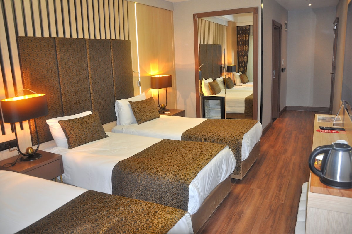 Quarto de hotel com duas camas, piso de madeira, um espelho grande e uma cafeteira em uma mesa lateral.