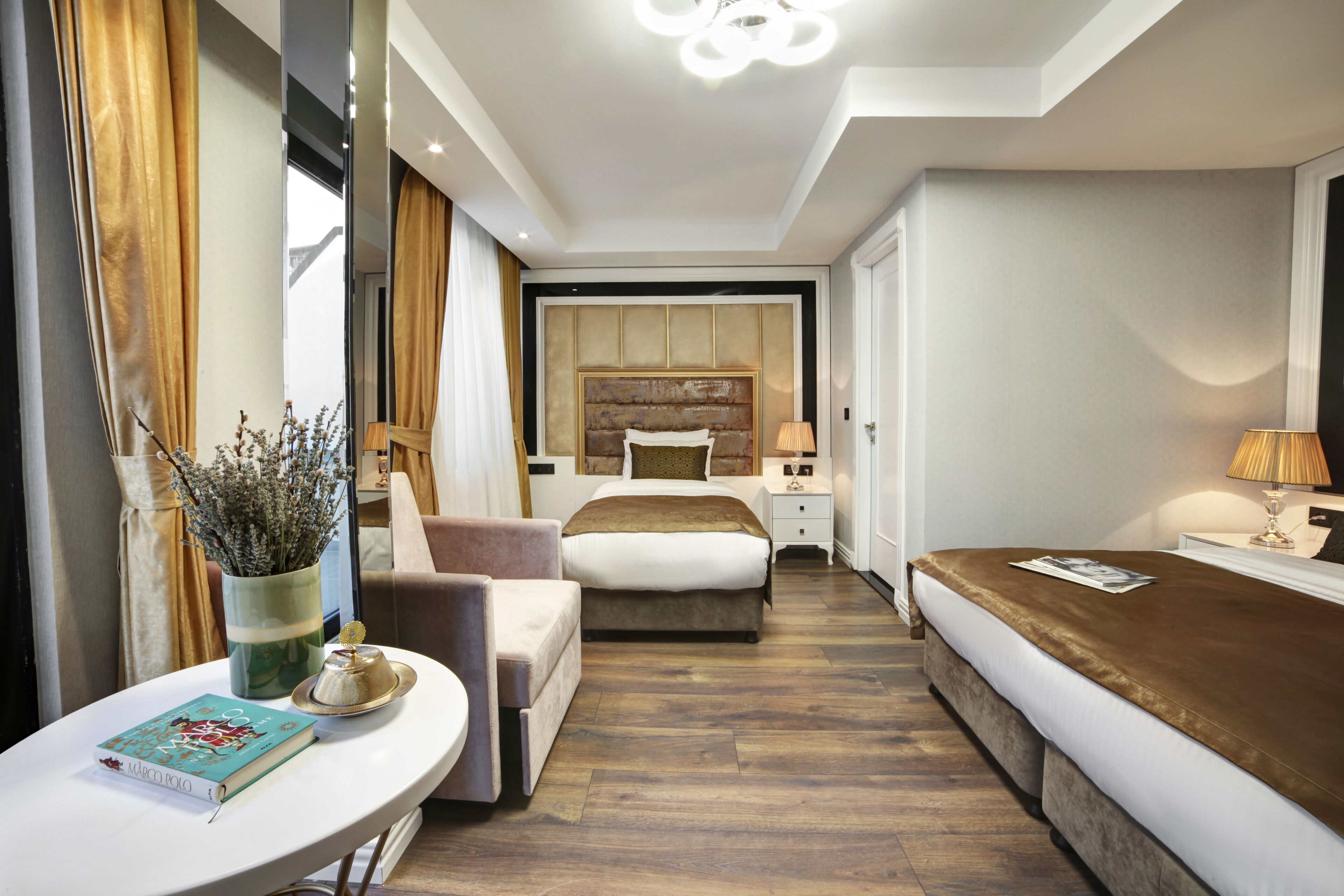 Ein Hotelzimmer mit einem Bett, Nachttischen, einem Sessel, einem kleinen Tisch mit einem Buch und einer Vase mit Blumen.