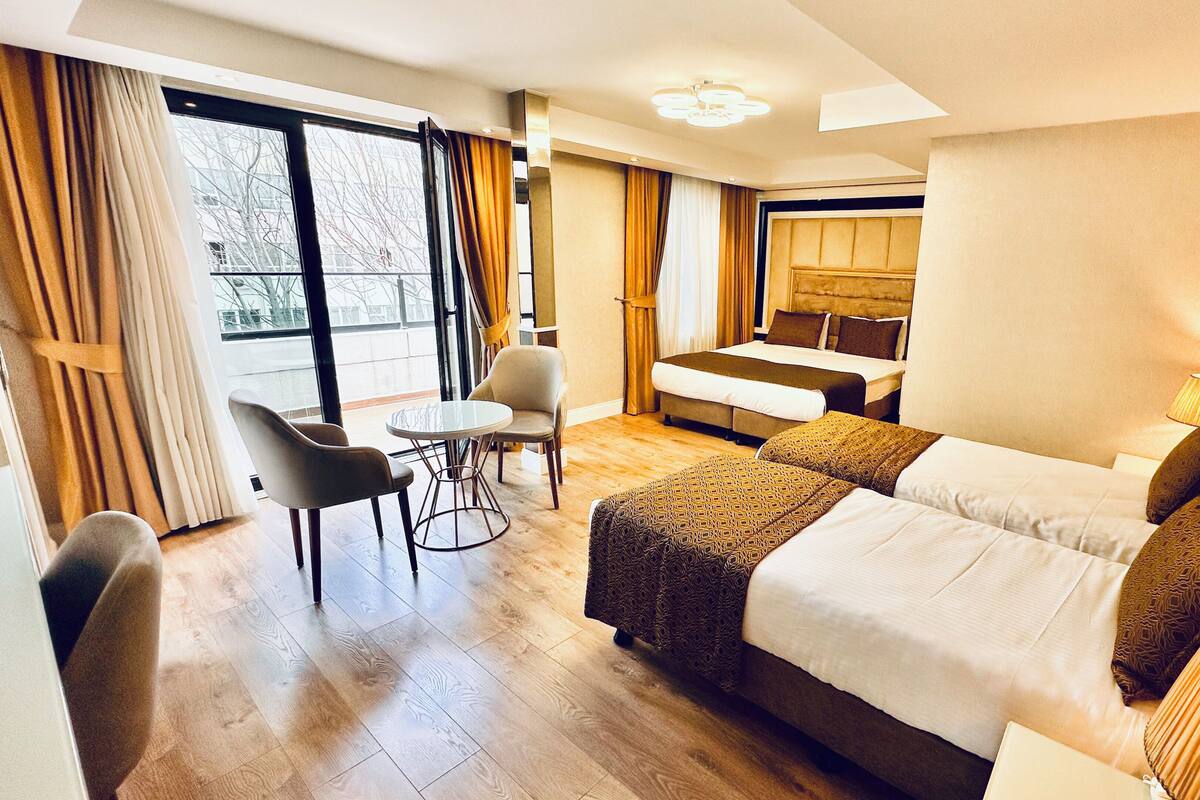 Quarto de hotel com cama, cadeira, mesinha e luminária.