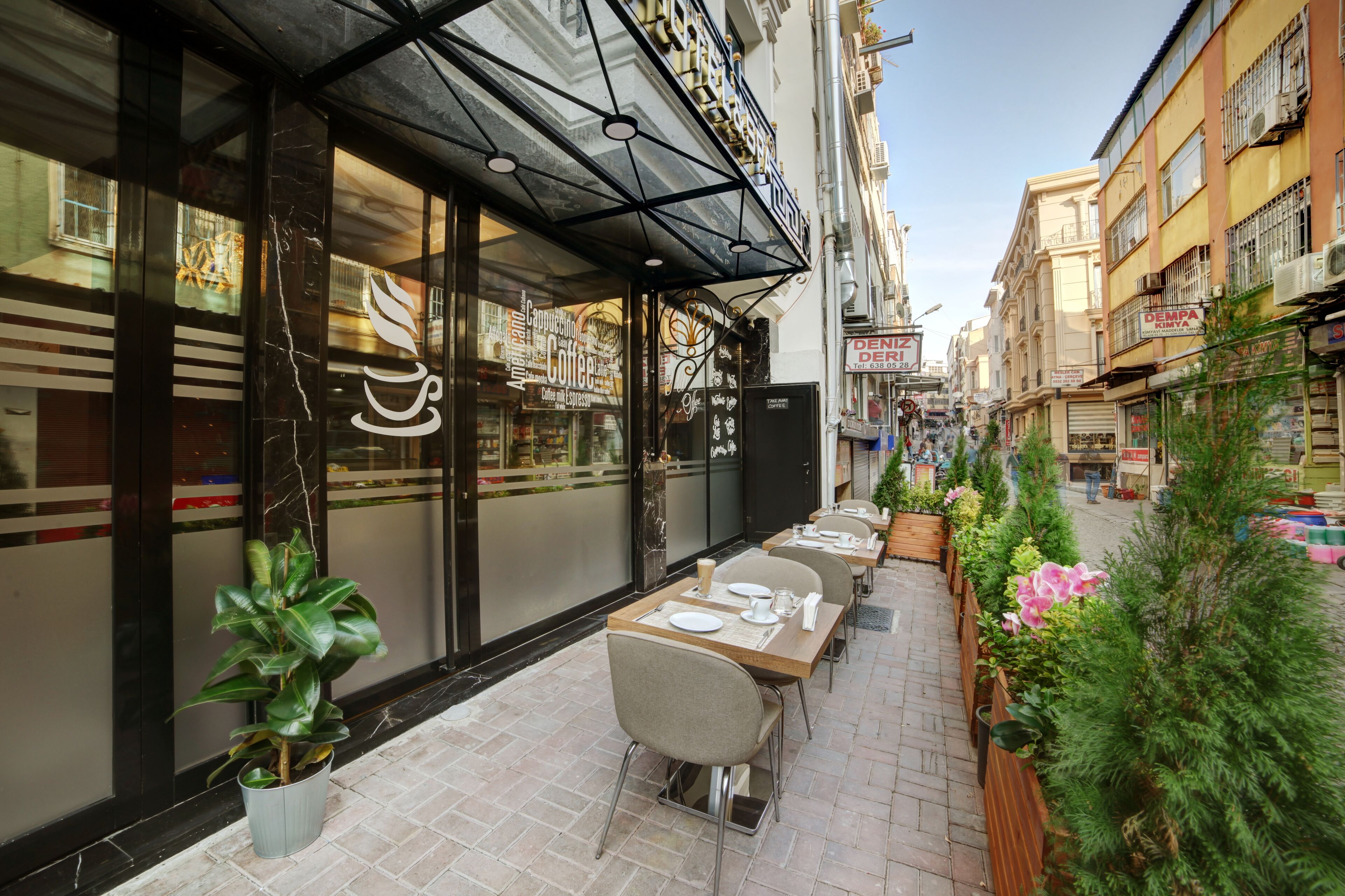 Un café con terraza, escaparate de vidrio y una calle estrecha flanqueada por edificios.
