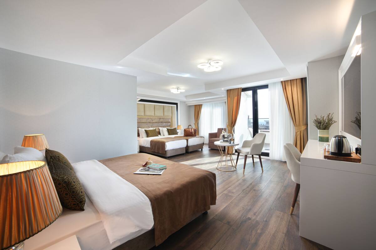 Quarto de hotel moderno com uma cama grande, uma escrivaninha com chaleira e vista para a cidade.